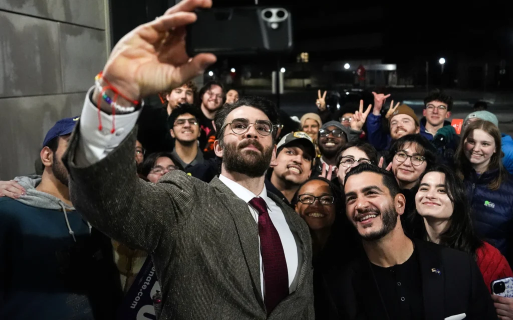 Hasan Piker (à gauche) et Abdul El-Sayed (au centre à droite), candidat progressiste à la primaire démocrate pour le Sénat américain dans le Michigan, prenant un selfie avec de jeunes fans à l’issue d’un meeting de campagne, à l’université du Michigan à Ann Arbor, dans le Michigan, le 7 avril 2026. (Crédit : Julia Demaree Nikhinson/AP Photo)
