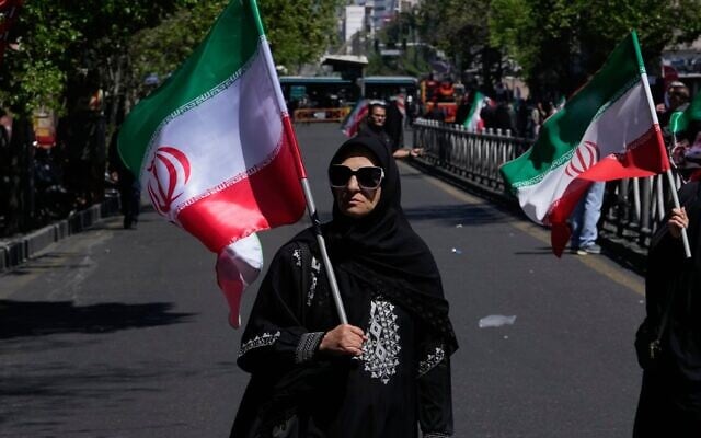 Une femme portant un drapeau iranien lors d'une cérémonie de deuil marquant le 40ᵉ jour depuis le décès du guide suprême iranien, l'ayatollah Ali Khamenei, éliminé lors des frappes américaines et israéliennes, à Téhéran, en Iran, le 9 avril 2026. (Crédit : Vahid Salemi/AP)