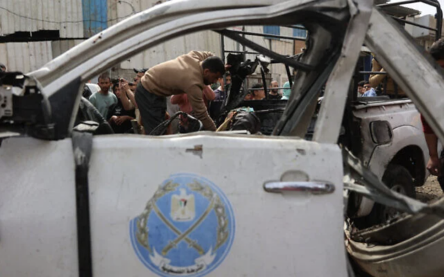Un Gazaoui inspectant les débris d'un véhicule de police détruit lors d'une frappe israélienne qui, selon le Hamas, aurait fait plusieurs morts, à Gaza-City le 14 avril 2026. (Crédit : Omar al-Qattaa/AFP)