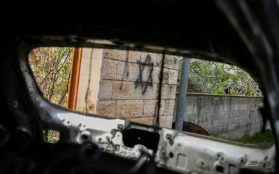 Des graffitis vus à travers la fenêtre d'une voiture incendiée suite à l'attaque par des résidents d'implantations de Deir al-Hatab, à l'est de Naplouse, en Cisjordanie, le 23 mars 2026. (Nasser Ishtayeh/Flash90)