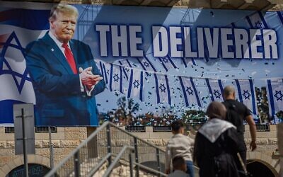 Des personnes marchant à côté d'une grande banderole représentant le président américain Donald Trump avec le slogan « Le Libérateur », à Jérusalem, le 19 avril 2026. (Crédit : Yonatan Sindel/Flash90)