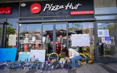 Devant la succursale de Pizza Hut, une femme allumant une bougie parmi des dizaines d’autres disposées au sol, tandis que des messages et des affiches recouvrent les vitrines, en hommage à Yemanu Binyamin Zelka, à Petah Tikva, le 25 avril 2026. (Crédit : Avshalom Sassoni/Flash90) Devant la succursale de Pizza Hut, une femme allumant une bougie parmi des dizaines d’autres disposées au sol, tandis que des messages et des affiches recouvrent les vitrines, en hommage à Yemanu Binyamin Zelka, à Petah Tikva, le 25 avril 2026. (Crédit : Avshalom Sassoni/Flash90)