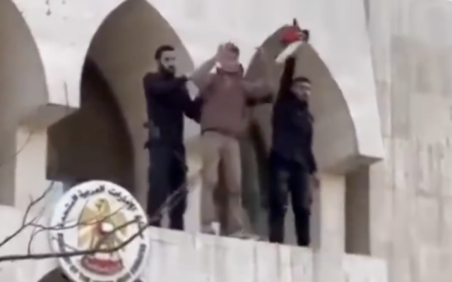 Un homme présenté par les médias arabes comme un agent de sécurité syrien (à droite) brandissant un drapeau "palestinien" qu'il a retiré  lors d'une manifestation anti-Israël du bâtiment de l'ambassade des Émirats arabes unis, à Damas, en Syrie, le 3 avril 2026. (Crédit : Capture d'écran/X ; utilisée conformément à l'article 27a de la loi sur le droit d'auteur)