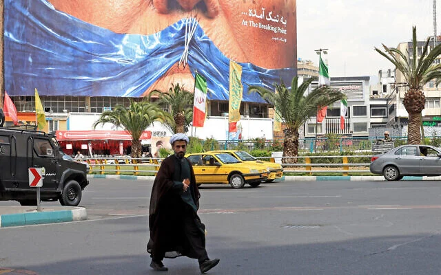Un religieux iranien passe devant un panneau anti-américain faisant référence au président Donald Trump et au détroit d’Ormuz, installé sur un bâtiment de la place Valiasr à Téhéran, le 2 mai 2026 (AFP)