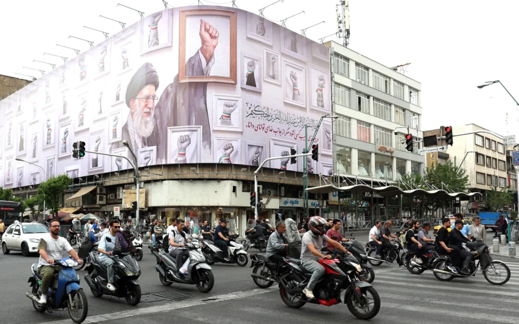 Des Iraniens passent devant un immense panneau d'affichage à l'effigie du guide suprême iranien Ali Khamenei, tué en février 2026 lors d'une attaque militaire menée par les États-Unis et Israël contre l'Iran, dans une rue de Téhéran, le 5 mai 2026. (Crédit : AFP)