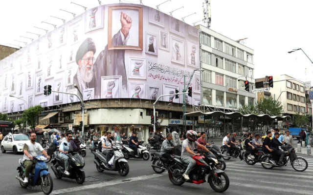 Des Iraniens passent devant un immense panneau d'affichage à l'effigie du guide suprême iranien Ali Khamenei, tué en février 2026 lors d'une attaque militaire menée par les États-Unis et Israël contre l'Iran, dans une rue de Téhéran, le 5 mai 2026. (Crédit : AFP)