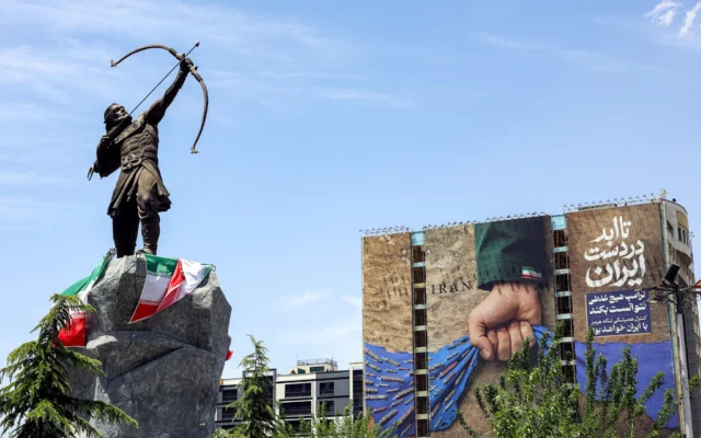 Une statue représentant Arash l’Archer, figure mythique perse qui, selon la tradition, aurait défini la frontière entre la Perse et les Turaniens, est exposée près d’un panneau d’affichage sur la façade d’un bâtiment représentant le détroit d’Ormuz, avec une légende en persan indiquant "Pour toujours entre les mains de l’Iran", sur la place Vanak à Téhéran, le 6 mai 2026. (Crédit:  AFP)