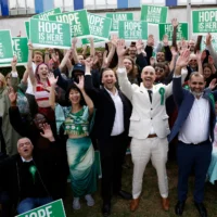 Le chef du Parti vert, Zack Polanski (au centre), célébrant avec le maire de Lewisham nouvellement élu par son parti, Liam Shrivastava (au centre à droite), et des partisans, devant le centre de dépouillement de Lewisham, au sud de Londres, le 8 mai 2026. (Crédit: Brook Mitchell / AFP)