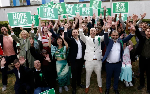 Le chef du Parti vert, Zack Polanski (au centre), célébrant avec le maire de Lewisham nouvellement élu par son parti, Liam Shrivastava (au centre à droite), et des partisans, devant le centre de dépouillement de Lewisham, au sud de Londres, le 8 mai 2026. (Crédit : Brook Mitchell/AFP)