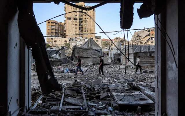 Des personnes marchent devant un immeuble résidentiel touché par une frappe israélienne la veille dans le quartier de Rimal à Gaza, le 16 mai 2026. (Crédit: Omar AL-QATTAA / AFP)