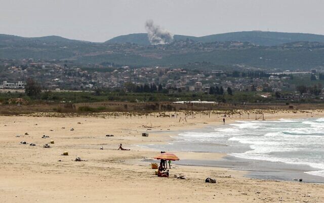 De la fumée s'élevant en arrière-plan après des frappes israéliennes visant le groupe terroriste chiite libanais du Hezbollah dans le village de Zibqin tandis que des personnes sont assises sur une plage à Tyr, dans le sud du Liban, le 17 mai 2026. (Crédit : Kawnat Haju/AFP)