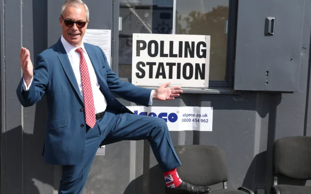 Le chef du Parti Reform britannique, Nigel Farage, montre ses chaussettes à son arrivée dans un bureau de vote à Walton-on-the-Naze, en Angleterre, le 7 mai 2026, pour voter aux élections locales. (Crédit: AP Photo/Richard Pelham)