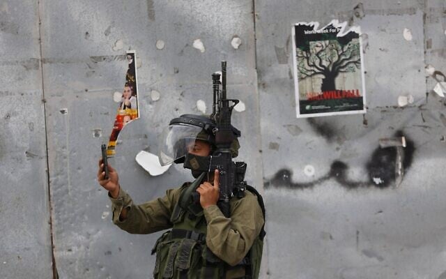 Ilustration : Un soldat israélien prenant une photo avec son téléphone portable lors d'affrontements avec des manifestants palestiniens, dans la ville de Bethléem, en Cisjordanie, le 13 octobre 2015. (Crédit : Nasser Shiyoukhi/AP)