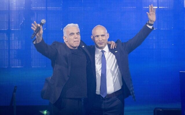 Le chef de l'opposition Yaïr Lapid (à gauche) et l'ancien Premier ministre Naftali Bennett s'étreignant lors d'un rassemblement de leur parti commun « BeYahad », à Tel Aviv, le 12 mai 2026. (Crédit : Miriam Alster/Flash90)