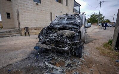 Un homme se tenant près d'une voiture incendiée et d'un graffiti tagué sur le mur d'une mosquée, que les Palestiniens attribuent à des résidents d'implantations israéliens extrémistes, dans le village de Jibya, au nord de Ramallah en Cisjordanie, le 15 mai 2026. (Crédit : Flash90)