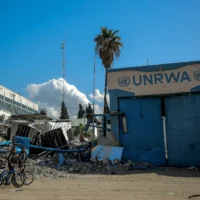 Deux Palestiniens passent à vélo devant le siège endommagé de l’Office de secours et de travaux des Nations unies pour les réfugiés de Palestine (UNRWA) à Gaza, le 15 février 2024 (Crédit: AFP)