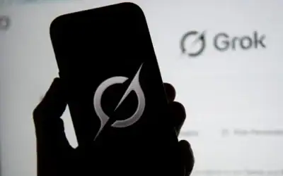 Sur cette illustration photographique, le logo de Grok apparaissant sur un téléphone portable à côté du site web affiché sur un écran d’ordinateur, à Bogota, le 12 février 2026. (Crédit : Pablo Vera/AFP)