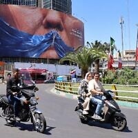 Le 10 mai 2026, des motos passent devant un panneau d'affichage anti-américain faisant référence au président Donald Trump et au détroit d'Ormuz, installé sur un immeuble de la place Valiasr à Téhéran. (Photo : ATTA KENARE / AFP)