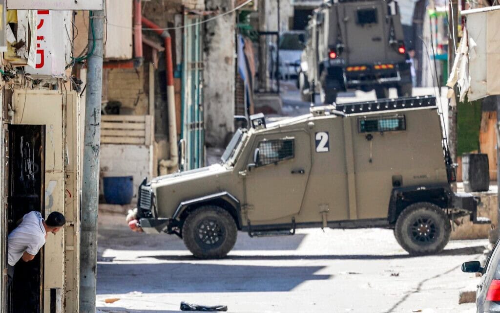 Un homme se mettant à l'abri tandis que des véhicules blindés de l'armée israélienne avancent dans les ruelles du camp de Balata, à l'est de Naplouse en Cisjordanie, lors d'une opération militaire israélienne, le 7 juin 2026 (Crédit : Jaafar Ashtiyeh/AFP)