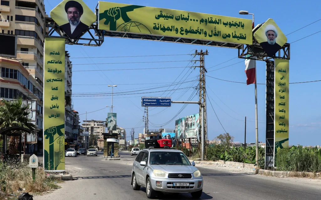 Une voiture chargée de valises quitte Tyr en passant devant une affiche du Hezbollah, dans le sud du Liban, le 9 juin 2026 (Crédit: KAWNAT HAJU / AFP) /
