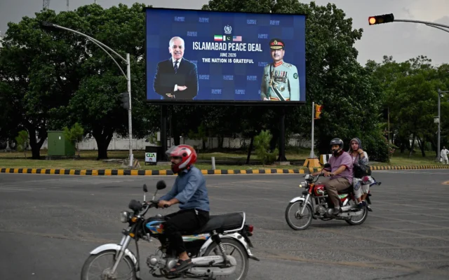 Des motos passent devant un panneau électronique représentant le Premier ministre pakistanais Shehbaz Sharif (à gauche) aux côtés du chef de l'armée et maréchal Syed Asim Munir, installé au bord d'une route à Islamabad le 17 juin 2026 (Crédit: Aamir QURESHI / AFP)