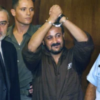 Marwan Barghouti, au centre, lève ses mains menottées en l'air lors de la première journée de son procès à Tel-Aviv, le 14 août 2002. (Crédit: AP/Brennan Linsley, archives)