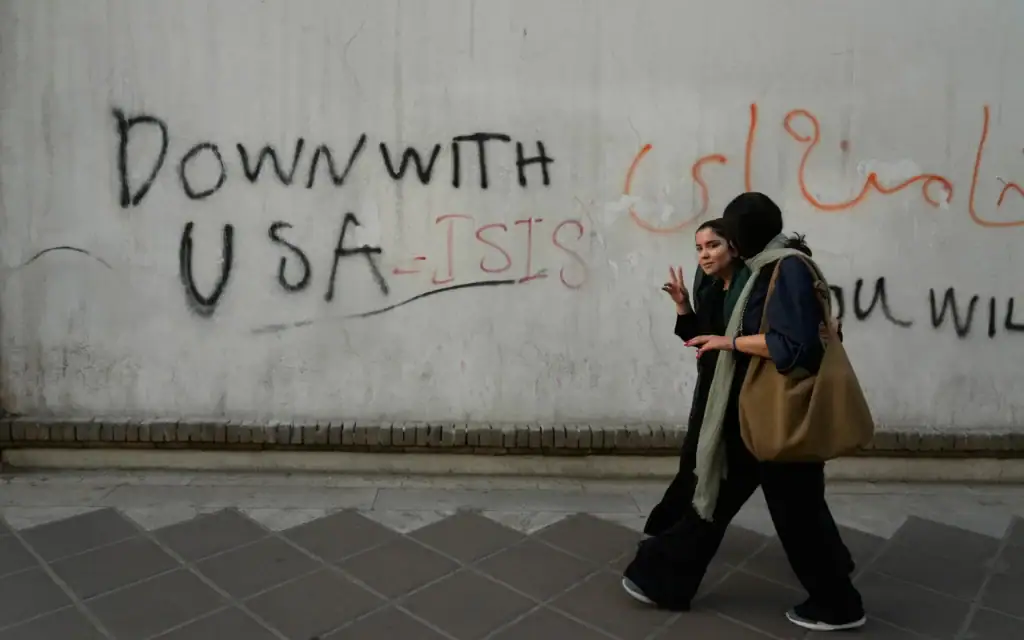 Une femme réagit devant l'objectif alors qu'elle passe devant un graffiti anti-américain peint sur le mur de l'ambassade britannique à Téhéran, en Iran, le 6 juin 2026. (Crédit: AP/Vahid Salemi)