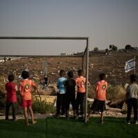 De jeunes garçons Palestiniens regardent un jeune résident d'implantation israélien après que leur ballon de football, tombé au-delà d'une clôture barbelée entourant un petit terrain près de l'implantation de Carmel, leur a été confisqué, dans le village bédouin d'Umm al-Khair, en Cisjordanie, le 12 mai 2026. (Crédit : AP Photo/Leo Correa)