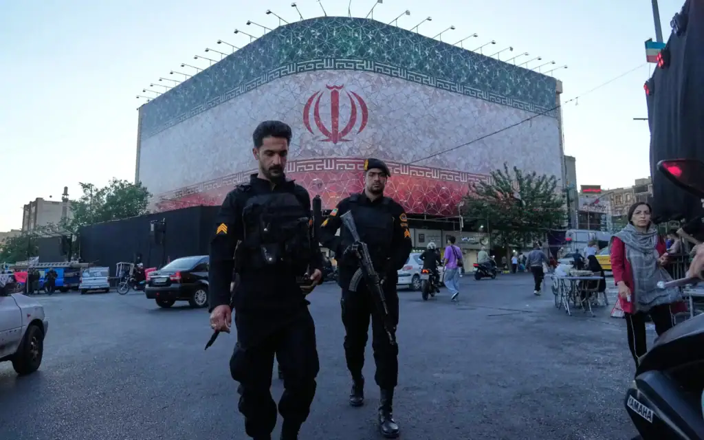 Des policiers marchant devant une immense banderole arborant le drapeau de la République islamique, sur la place de la Révolution islamique, à Téhéran, en Iran, le 14 juin 2026. (Crédit : Vahid Salemi/AP) Des policiers marchant devant une immense banderole arborant le drapeau de la République islamique, sur la place de la Révolution islamique, à Téhéran, en Iran, le 14 juin 2026. (Crédit : Vahid Salemi/AP)
