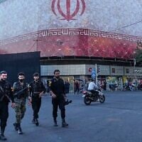 Des policiers marchant devant une bannière représentant le drapeau du régime iranien, sur la place de la Révolution islamique, à Téhéran, en Iran, le 14 juin 2026. (Crédit : Vahid Salemi/AP)
