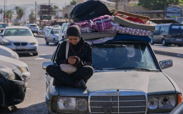 Une femme déplacée consulte son téléphone portable alors qu'elle attend de pouvoir retourner dans son village, après l'annonce d'un premier accord de cessez-le-feu entre les États-Unis et l'Iran, dans la ville portuaire de Sidon, au sud du Liban, le 15 juin 2026. (Crédit : AP/Mohammed Zaatari)