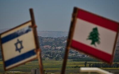 Des drapeaux israéliens et libanais sont visibles dans une zone proche de la frontière, avec en arrière-plan des bâtiments détruits dans le sud du Liban, vus depuis le nord d'Israël, le 15 juin 2026. (Crédit : Leo Correa/AP)