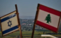 Des drapeaux israéliens et libanais sont visibles dans une zone proche de la frontière, avec en arrière-plan des bâtiments détruits dans le sud du Liban, vus depuis le nord d'Israël, le lundi 15 juin 2026. (Crédit: AP/Leo Correa)