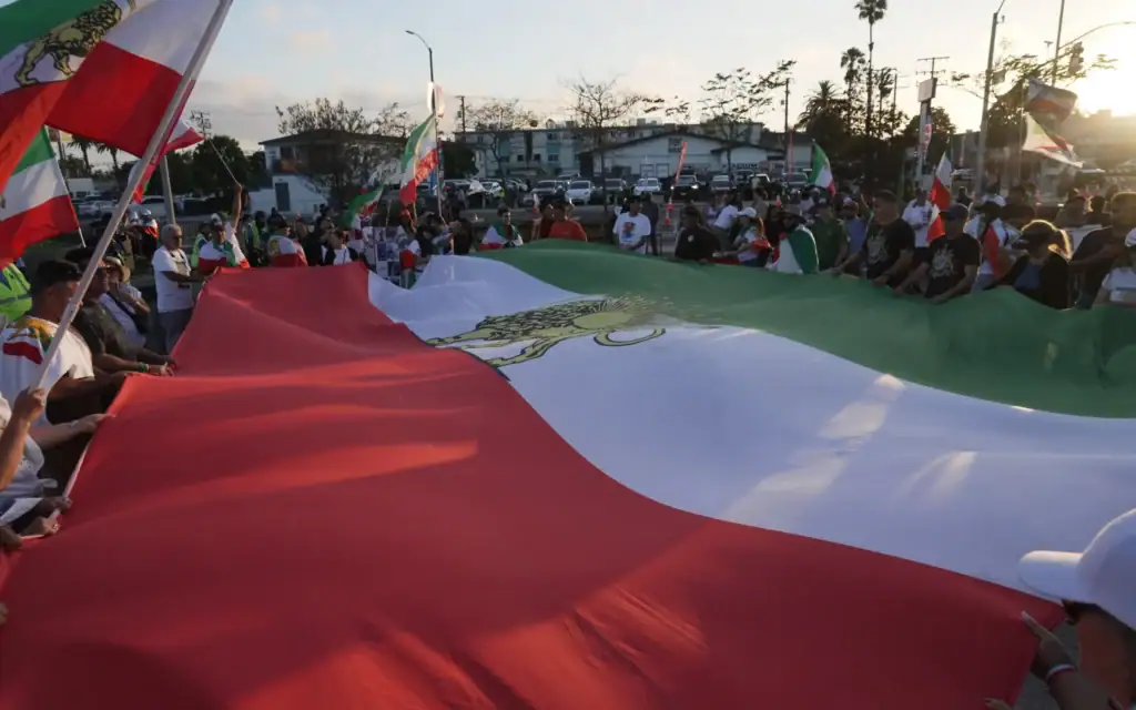 Des personnes déploient un grand drapeau iranien d'avant la révolution lors d'une manifestation devant le stade de Los Angeles avant le match de football de la Coupe du monde du groupe G opposant l'Iran à la Nouvelle-Zélande à Inglewood, en Californie, près de Los Angeles, le 15 juin 2026. (Crédit: AP/Ty ONeil)