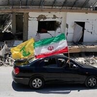 Des habitants déplacés brandissant un drapeau de la Révolution islamique et un drapeau du groupe terroriste chiite libanais du Hezbollah en passant devant un bâtiment détruit lors d’une précédente frappe aérienne israélienne, dans le village de Chehabiyeh, au sud du Liban, le 16 juin 2026. (Crédit : Mohammed Zaatari/AP)