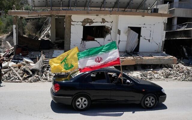 Des habitants déplacés brandissant un drapeau de la Révolution islamique et un drapeau du groupe terroriste chiite libanais du Hezbollah en passant devant un bâtiment détruit lors d’une précédente frappe aérienne israélienne, dans le village de Chehabiyeh, au sud du Liban, le 16 juin 2026. (Crédit : Mohammed Zaatari/AP)