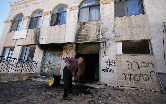 Un homme nettoyant les décombres devant une inscription en hébreu sur le mur, qui dit « vengeance, salut aux arrêtés, peuple, réveillez-vous », dans l'une des mosquées de Cisjordanie qui ont été vandalisées et partiellement incendiées par des résidents d'implantations pendant la nuit, dans le village de Jiljilya, au nord de Ramallah, le 17 juin 2026. (Crédit : Majdi Mohammed/AP)