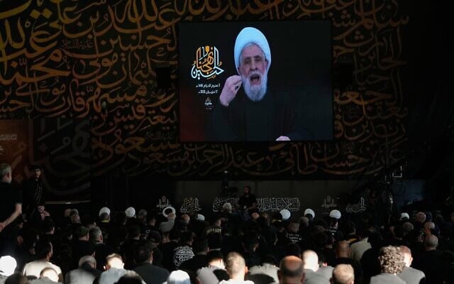 Le chef du groupe terroriste chiite libanais du Hezbollah, le cheikh Naïm Qassem, apparaissant sur un écran lors d'un sermon marquant le premier jour de l'Achoura, devant la tombe de l'ancien chef du Hezbollah, Sayyed Hassan Nasrallah (à gauche), à Beyrouth, au Liban, le 17 juin 2026. (Crédit : Hussein Malla/AP Photo)
