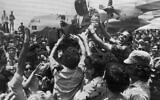 Une foule en liesse à l’aéroport Ben Gurion soulevant un soldat de l’équipe de sauvetage qui a libéré les otages kidnappés en Ouganda plus tôt dans la journée, le 4 juillet 1976. À l’arrière-plan se trouve l’avion de transport C-130 qui a pris part au raid. Le visage du sauveteur est masqué pour des raisons de sécurité. (Crédit : AP Photo/Pool)