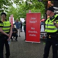 Des policiers patrouillant tandis qu'un manifestant se tient près d'une banderole devant la salle où Ye, le rappeur anciennement connu sous le nom de Kanye West, doit se produire, à Arnhem, aux Pays-Bas, le 6 juin 2026. (Crédit : Mouneb Taim/AP)