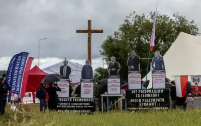 Des banderoles portant les inscriptions "Je ne m’excuse pas pour Jedwabne, que les coupables s’excusent" et "Achevez les exhumations, mettez fin aux calomnies contre les Polonais, au mensonge de Jedwabne", accompagnées de silhouettes représentant le grand rabbin de Pologne Michael Schudrich et d’anciens présidents polonais, sont visibles à côté d’un crucifix installé lors d’un rassemblement de partisans d’extrême qui remettent en cause la culpabilité des citoyens polonais dans le massacre de Jedwabne, en marge d’une cérémonie officielle au mémorial du massacre de Jedwabne rendant hommage à la mémoire des habitants juifs de la ville assassinés le 10 juillet 1941 par leurs voisins polonais, à Jedwabne, dans le nord-est de la Pologne, le 10 juillet 2026. (Crédit: Wojtek RADWANSKI / AFP)