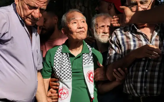 Kozo Okamoto (au centre) — seul survivant de l’unité commando de trois hommes de l’« Armée rouge japonaise » (JRA) qui a tué 26 personnes lors d’un attentat contre l’aéroport israélien de Lod le 30 mai 1972 — assiste à une cérémonie organisée par des militants palestiniens pour marquer le 50e anniversaire de l’attentat terroriste de Lod, à Beyrouth, la capitale du Liban, le 30 mai 2022. (Crédit: JOSEPH EID/AFP)