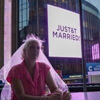 Une fan de Taylor Swift, coiffée d'un voile de mariée, est assise dans un restaurant situé à proximité du Madison Square Garden de New York, où une pancarte « JUST&T MARRIED » est affichée lors du mariage de Taylor Swift avec la star de la NFL Travis Kelce, le 3 juillet 2026. (Crédit : AP Photo/Ryan Murphy)