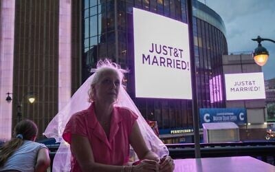 Une fan de Taylor Swift, coiffée d'un voile de mariée, est assise dans un restaurant situé à proximité du Madison Square Garden de New York, où une pancarte « JUST&T MARRIED » est affichée lors du mariage de Taylor Swift avec la star de la NFL Travis Kelce, le 3 juillet 2026. (Crédit : AP Photo/Ryan Murphy)