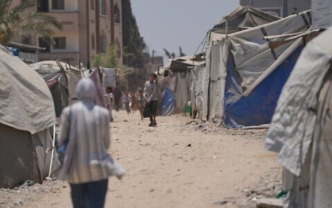Des Palestiniens déplacés marchent entre des tentes à Deir al-Balah, au centre de la bande de Gaza, le 4 juillet 2026. (Crédit : AP Photo/Abdel Kareem Hana)
