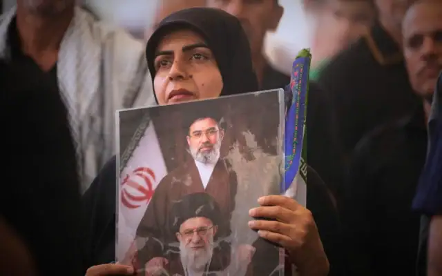 Une femme tient un portrait représentant le Guide suprême iranien, l’ayatollah Mojtaba Khamenei (en haut), et son défunt père, l’ayatollah Ali Khamenei, lors du cortège funèbre de ce dernier à l’intérieur du mausolée de l’imam Ali à Najaf, en Irak, le 8 juillet 2026. (Crédit: AP/Hadi Mizban)