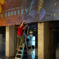Un employé installe une affiche peinte à la main, réalisée par l’artiste Virginia Axioti, pour le prochain film de Christopher Nolan, L’Odyssée, avec Matt Damon dans le rôle d’Ulysse, devant le cinéma Athinaion d’Athènes, le 11 juillet 2026. Illustration (Crédit : AP)