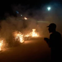 Un Palestinien se tient près d'un feu de broussailles allumé sur le bord de la route pour empêcher une attaque de résidents d'implantations israéliens dans le village de Sinjil, en Cisjordanie, le 17 juillet 2026. (AP/Leo Correa)