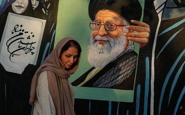 Une femme passant devant une fresque représentant le portrait de l'ayatollah Ali Khamenei, ancien guide suprême iranien, tué lors de l'attaque menée par les États-Unis et Israël le 28 février, dans le centre-ville de Téhéran, en Iran, le 18 juillet 2026 (Crédit : Vahid Salemi/AP)