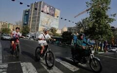 Un homme roulant à moto tandis que des garçons font du vélo, dans le centre-ville de Téhéran, en Iran, le 22 juillet 2026. (Crédit : Vahid Salemi/AP)